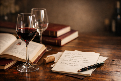 Närbild på vinglas med rödvin bredvid öppna vinböcker och anteckningar